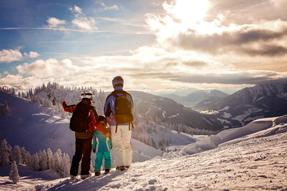 Happy family in winter clothing at the ski resort, winter time, watching at mountains in front of them