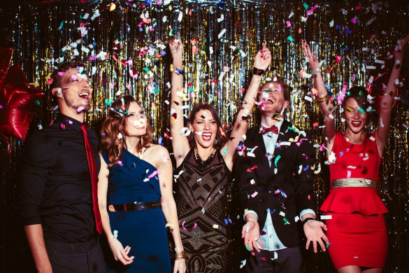Young people wearing elegant clothes celebrating or having party in front of fringe curtain. They are dancing, smiling and having fun, confetti is in the air, dancing in night club.