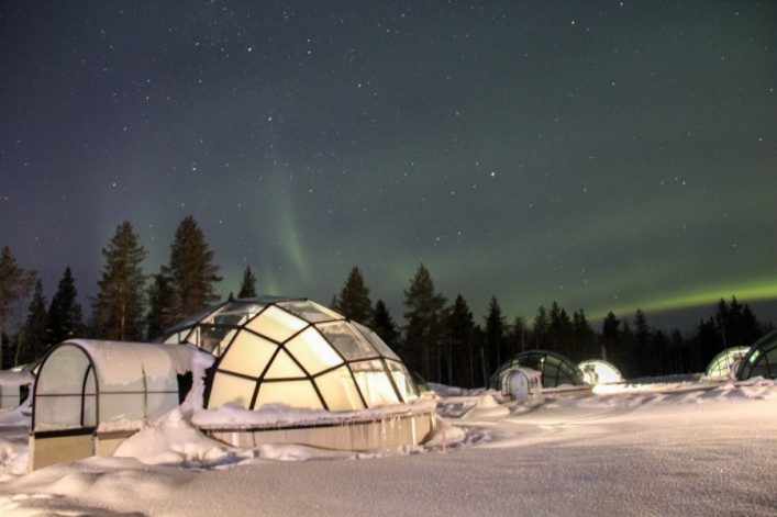 Glasiglu im Schnee. Im Himmel sind grüne und violette Polarlichter zu sehen.