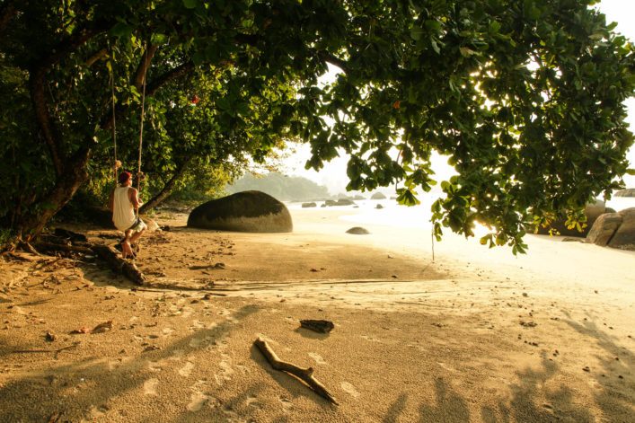 man on a swing at the beach in sunset; Malaysia.