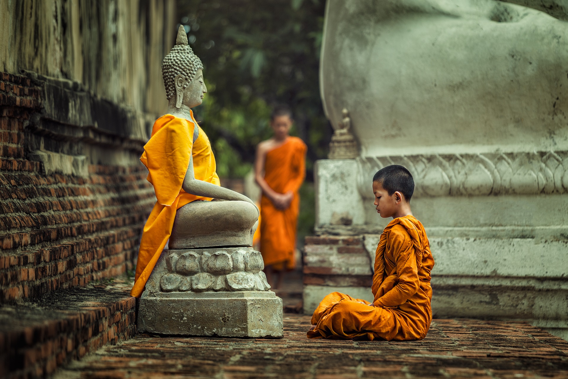 Ein junger Mönch vor einer Buddhastatue in Kambodscha