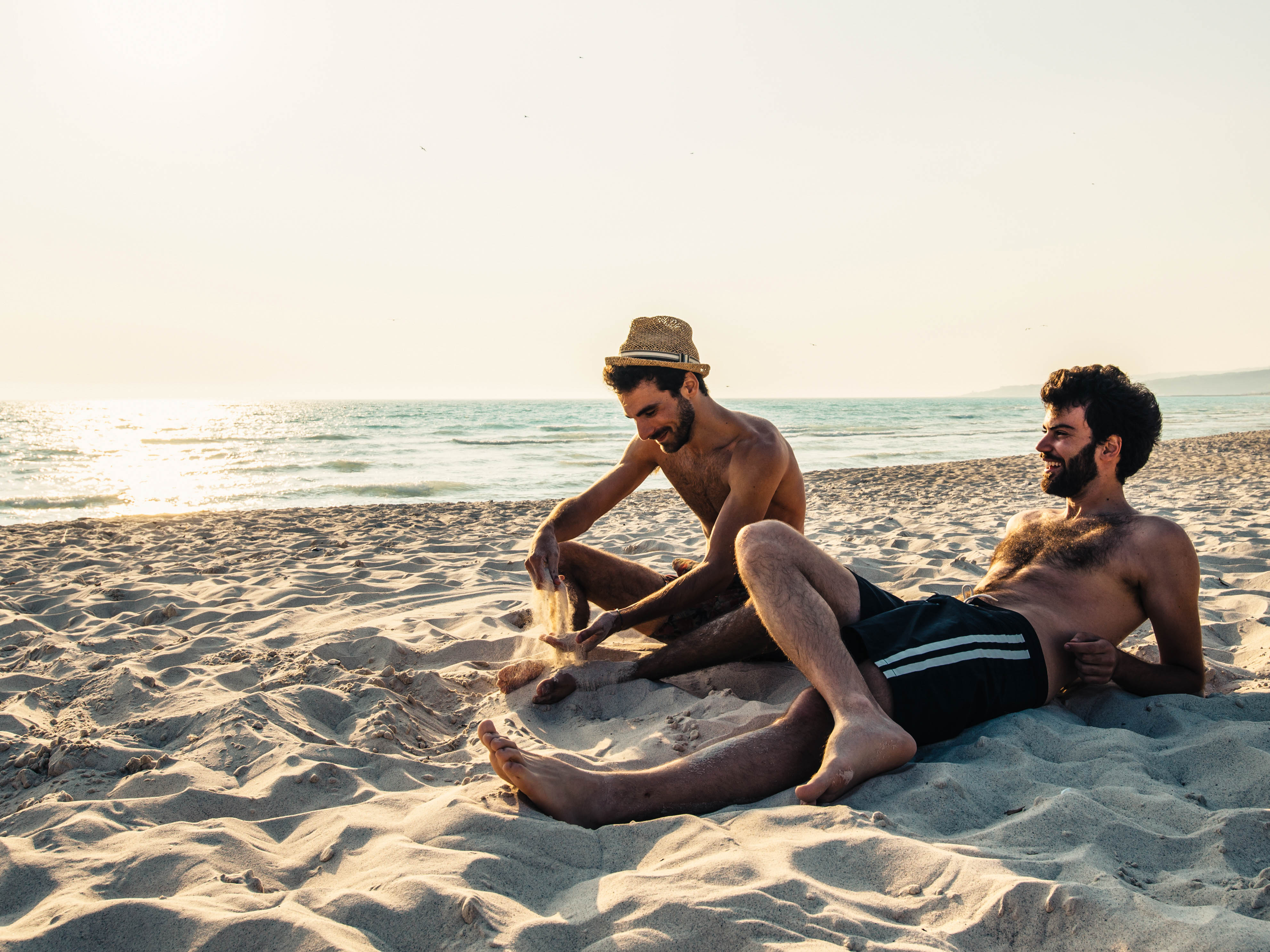 Zwei Männer liegen im Sand und lachen 