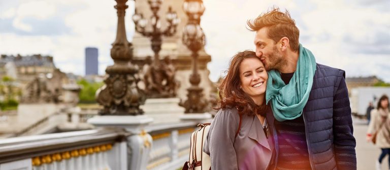 Ein Paar umarmt sich liebevoll auf einer Brücke in Paris; ideal für ein romantisches Valentinstagswochenende in einem der nahen Hotels.