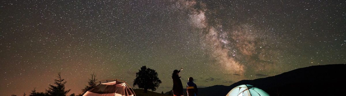 Mother and son tourists resting at camping in mountains at night sky full of stars and Milky way