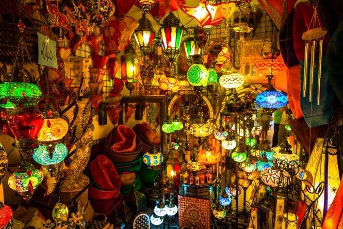 Bunte Lampen und Stoffe in einem Marktstand in Marrakesch, atmosphärisch beleuchtet, versprechen eine lebendige Souk-Erfahrung.