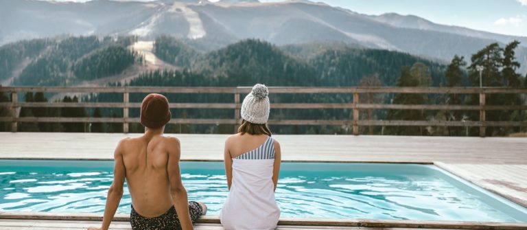 Entspannung pur in Österreichs Wellnesshotels: Zwei Personen sitzen am Rand eines Außenpools, blicken auf idyllische Berge.