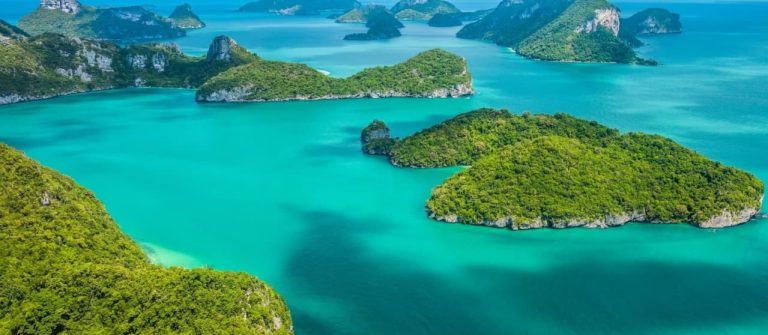 Gruppe von grünen, bewaldeten Inseln verteilt im türkisfarbenen, ruhigen Meer, unter blauem Himmel mit vereinzelten Wolken, blick von erhöhter Position, Wasser umgibt die Inseln, Hintergrund bis zum Horizont.