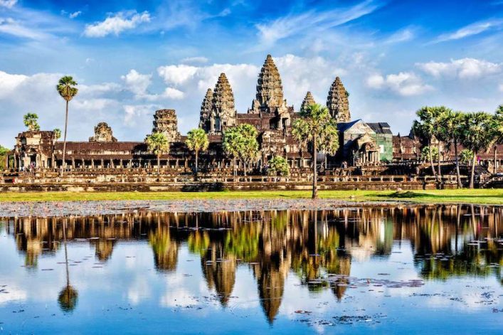 Angkor Wat Tempelanlage in Kambodscha bei Tag: Das alte Steingebäude mit Türmen, die an Tannenzapfen erinnern, spiegelt sich im Wasser.