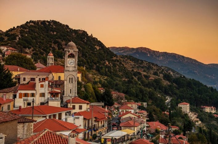 Traditional-houses-of-Dimitsana-village-with-the-tall-clock-tower-dominating-against-a-cloudy-sky.-Arcadia-Peloponnese-Greece-shutterstock_1171086256