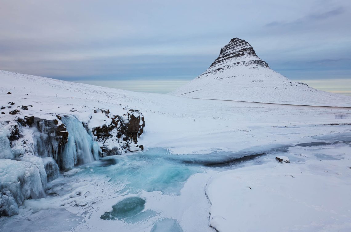 Island-Landschaft-Winterpanorama-Kirkjufell-Berg-von-Schnee-mit-Wasserfall-bedeckt-iStock-1148997684