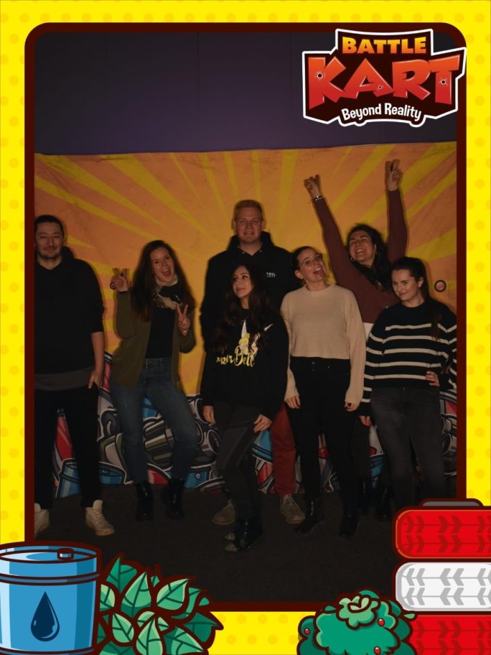 Sieben fröhliche Personen posieren bei BattleKart in Wien vor einer Wand mit Graffiti. Über ihnen prangt das Logo