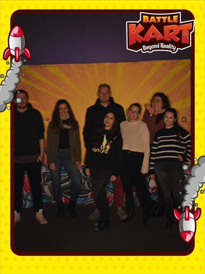 Gruppe lächelnder Menschen steht vor BattleKart-Logo in Wien; im Hintergrund eine grafitiähnliche Wandgestaltung, umrahmt von Cartoon-Raketen.