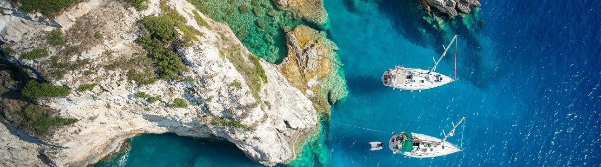 Türkisblaues Meer mit Booten an einer Felsbucht auf Korfu Griechenland