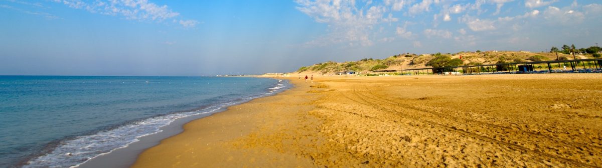 Einer der schönsten Strände in Side, umgeben von klarem Meer, goldenem Sand und sanften Dünen, mit vereinzelten Spaziergänger