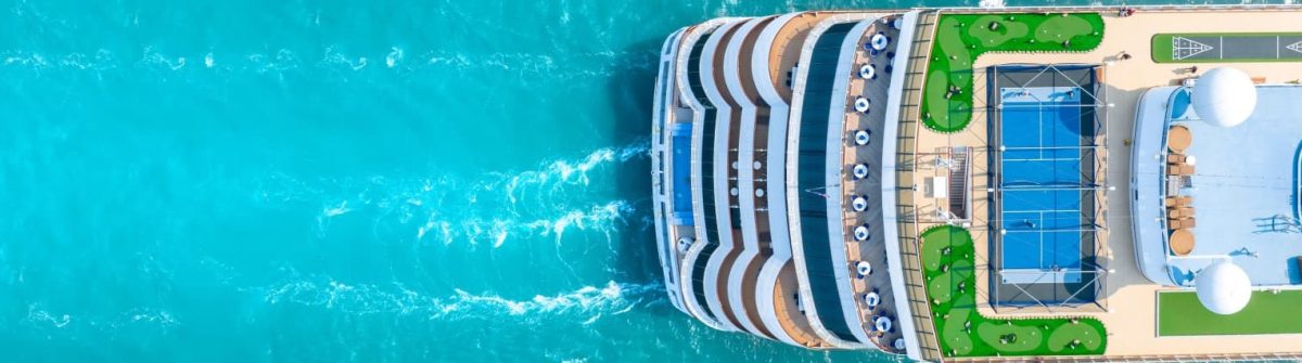 Ein großes Kreuzfahrtschiff von oben auf türkisfarbenem Meer, mit mehreren Decks, Pools und Sonnenliegen.