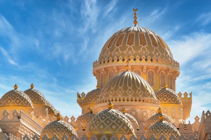 Goldverzierte Kuppeln der Al-Mina-Moschee erstrahlen vor blauem Himmel in Hurghada, feine Ornamente zeichnen sich ab.