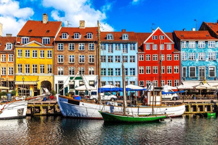 Bunte Reihenhäuser am Nyhavn-Kanal in Kopenhagen, ideal für eine Städtereise im September. Segelschiffe schmücken das Wasser, Cafés im Freien laden zum Verweilen ein.
