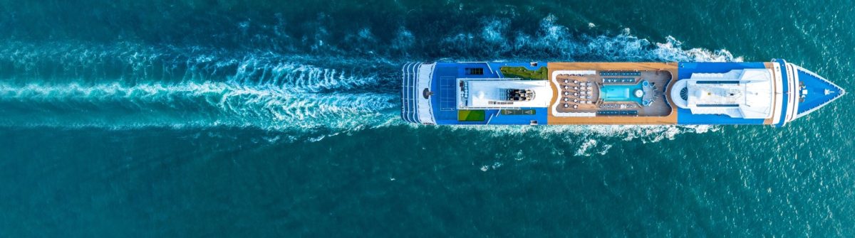 Ein großes Kreuzfahrtschiff aus Vogelperspektive schneidet sich seinen Weg durch das tiefblaue Meer, hinterlässt eine aufgewühlte Gischtspur. Deck mit Pools sichtbar.
