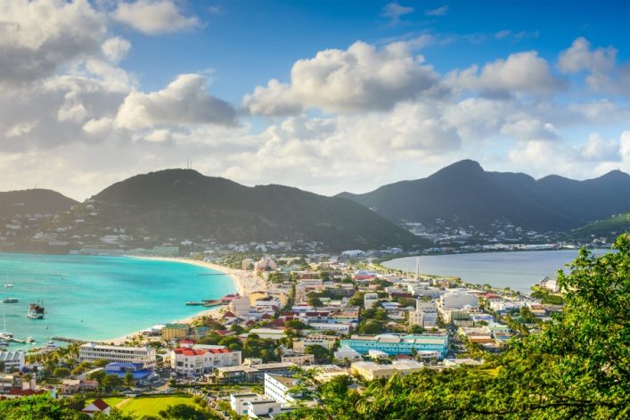 Luftaufnahme von Philipsburg auf St. Martin. Die Insel wird hier sehr schmal. Rechts und links ist Meer. Auf der Insel stehen bunte Häuser. Im Hintergrund sind Berge.