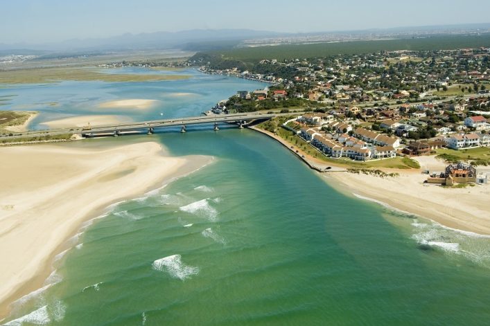 Luftaufnahme von Port Elizabeth, Südafrika, mit Strand, Mündung, Brücke und Wohngebieten, umgeben von grüner Landschaft.