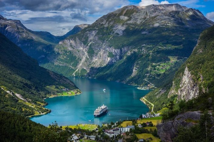 Blick auf den Geirangerfjord mit einem Kreuzfahrtschiff. Da Bild wird umrahmt von grüner Natur und Bergen.